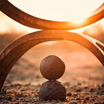 Beliefs and Valuies: Two rocks on a beach balancing under an arch while the sun sets.